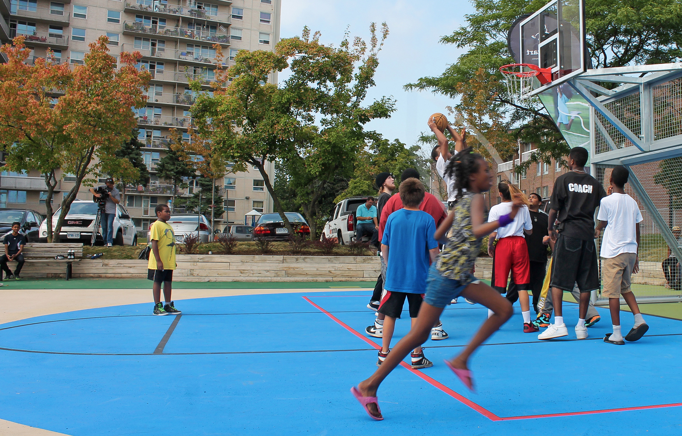 Court side photograph of children gathered under the net, playing a game of basketball on the Storefront Courts.